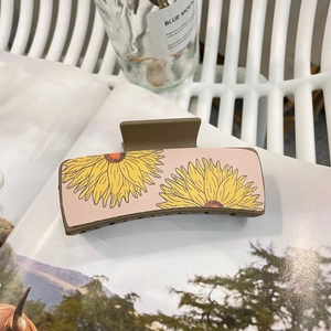 Detail shot of a square hair claw clip featuring yellow sunflower patterns on a pink background