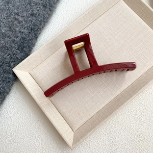 Macro detail of dark red large hair claw clip with golden spring on textured background