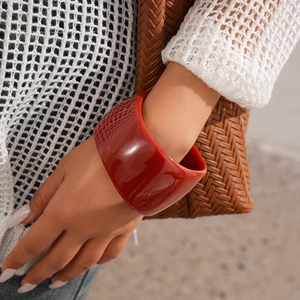 Close-up of a wide burgundy resin bangle on a wrist with luxury fashion aesthetics