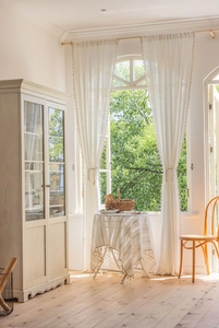 Detail of off-white lace curtains with delicate tassels in a warm French country setting