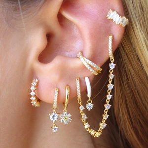 Detail of stacked gold earrings with snowflake and heart charms and cubic zirconia studs