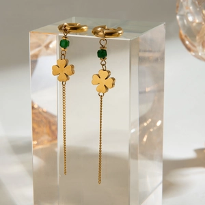Detail of gold clover earrings with green beads and long tassels on clear cube