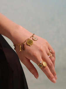 Macro shot of gold charm bracelet with fish pendants and embossed sun pattern rings on hand