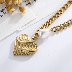 Detail of golden heart pendant with leaf texture and pearl on a double layer steel chain