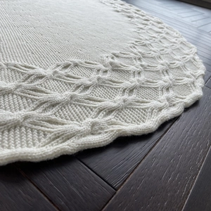 Knitted ivory Christmas tree skirt with wavy borders and diamond pattern on wood floor