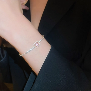 Detail of gold bracelet with rectangular pink zircon worn over a black blazer sleeve