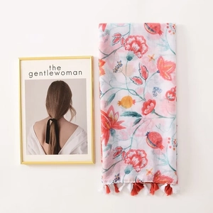 Floral pomegranate print scarf with red tassels hanging in a minimalist indoor setting