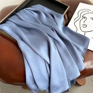 Close-up of elegant blue silk scarf folded on a leather chair with soft texture and sheen