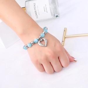 Detail of beaded bracelet with light blue opal beads and silver heart charm on wrist