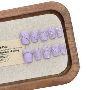 Short lavender press-on nails with silver metallic lines and pearls on a wooden tray