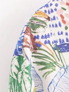 Detail of vibrant tropical leaf print and textured woven fabric on women's shirt shoulder