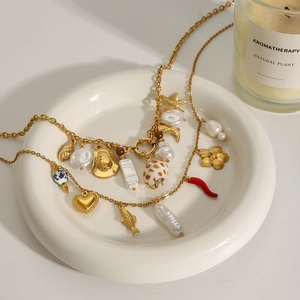 Golden stainless steel necklace with pearl heart and various charms on a ceramic plate