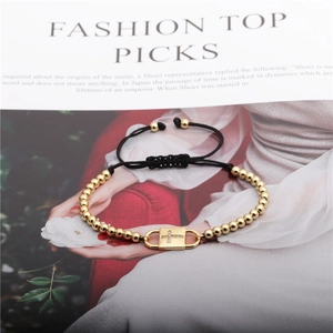 Detail view of gold bead bracelet featuring a zircon cross charm with black braided rope cord