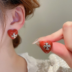 Detailed view of red heart earrings with silver cross inlay worn by a female model