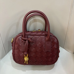 Detail of burgundy woven leather mini handbag with gold knot charm and handle