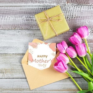 Flat lay of pink Mother's Day card with floral pattern, envelope and tulips on wood