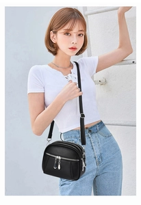 Close-up of black PU leather crossbody bag with multiple zippers shown on a model