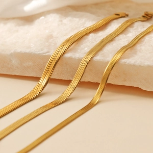 Three gold stainless steel flat snake chain bracelets in various widths on stone