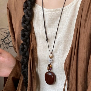 Ethnic style resin pendant necklace with reddish-brown beads worn on linen clothing