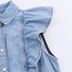 Detail van lichtblauwe denim stof met ruches aan de mouwen en witte metalen knopen