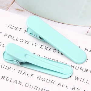 Detail of two mint blue matte finish metal duckbill hair clips on artistic paper