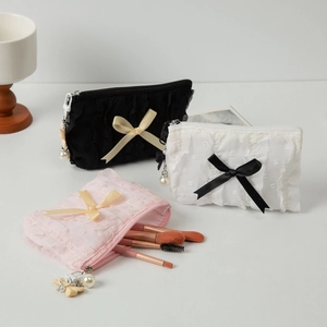 Three bow cosmetic bags in black, white, and pink with pearl zipper pulls and brushes