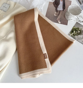Close-up of brown knit scarf with beige contrast trim and leather brand tag detail