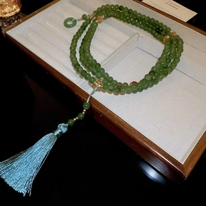 Détail d'un collier de perles vertes avec accents dorés et pompon en soie bleu clair