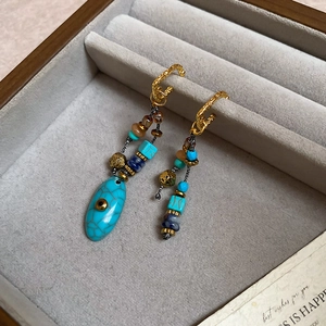 Dettaglio di orecchini vintage asimmetrici con perline e pietre turchesi in scatola