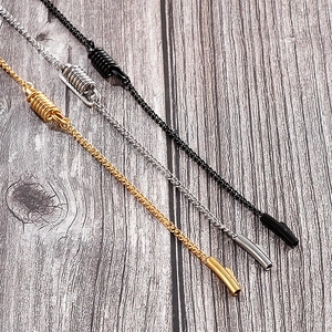 Close-up of titanium steel spring necklaces in gold, silver, and black on wood background