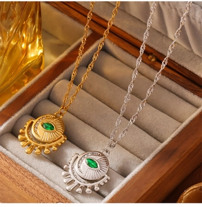 Detail of eye pendants in gold and silver with green zircon stones on velvet box