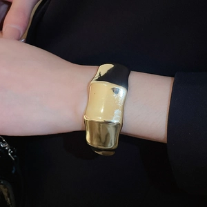 Detail of a wide golden cuff bracelet featuring a textured fluid surface on model