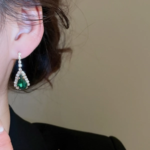 Nahaufnahme goldener Ohrring mit grünem Wassertropfen-Edelstein und Diamanten am Ohr