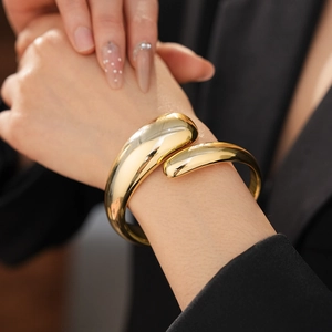Close-up of gold chunky liquid metal cuff bracelet worn on wrist over black blazer