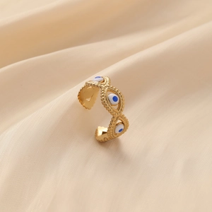 Gold-plated open ring with blue evil eye motifs on soft beige silk fabric background