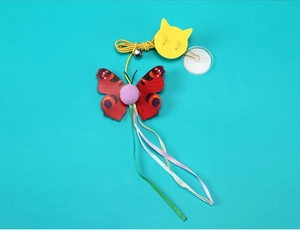 Hanging door cat toy featuring red butterfly wings, purple pom-poms and colorful ribbons