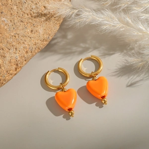 Vue détaillée de créoles dorées avec pendentifs cœur orange sur un socle en pierre
