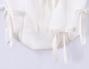 Detail of elegant white satin top featuring multiple decorative bow ties and smooth texture