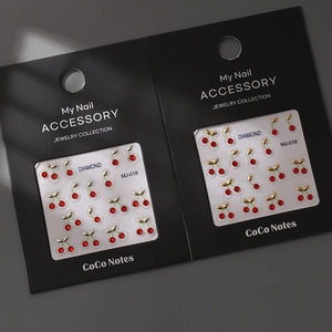 Detailed view of red cherry nail art charms with sparkling rhinestones and gold leaves