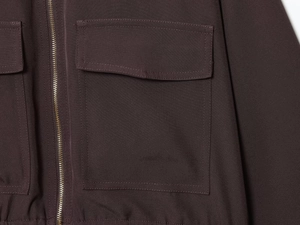 Détail d'une veste marron avec texture tissée, fermeture éclair et poche plaquée