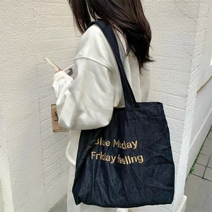 Detail of dark blue denim tote bag featuring golden embroidered text and durable canvas texture