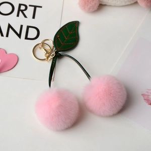 Close-up of pink faux rabbit fur cherry keychain with green leather leaves and gold clasp
