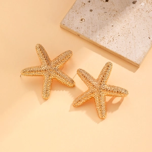 Macro detail of golden starfish earrings with lifelike relief texture on stone background