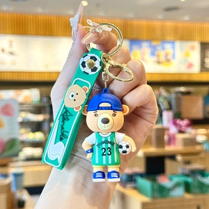 Close-up of a soccer bear mascot keychain in green jersey and blue hat with strap