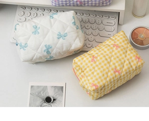 Quilted cosmetic bags with bow prints and checkered patterns on a bright office desk