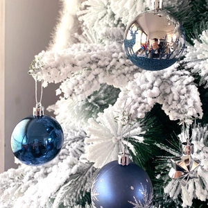 Close-up of blue Christmas ornaments with snowflakes and deer motifs on a snowy tree