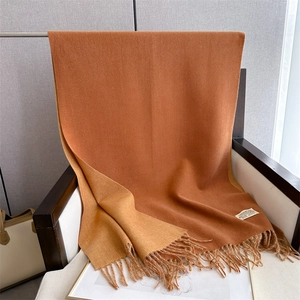 Detailed close-up of two-tone camel and caramel scarf with fringe and fabric label