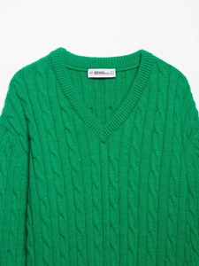 Detail of bright green V-neck cable knit sweater with ribbed collar and woven brand label