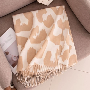 Stylish cream faux cashmere scarf with beige cow print and fringes on a grey sofa