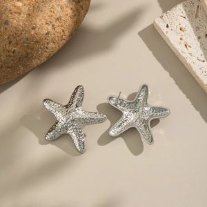 Elegantes pendientes de estrella de mar plateados con textura mate sobre piedra